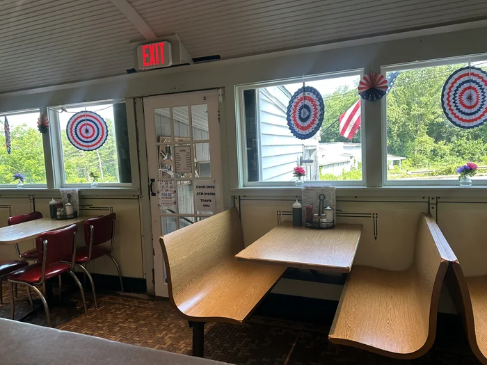 A corner booth with curved wooden benches beneath the windows, red chrome chairs at a table alongside.