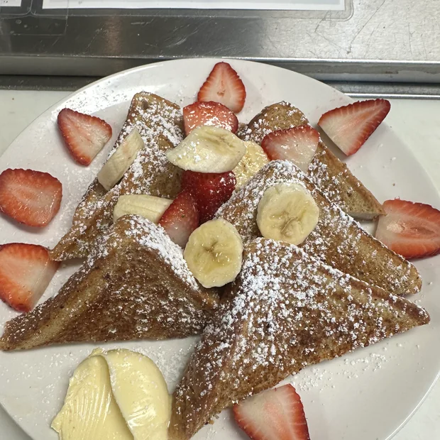 Banana bread french toast, cut into triangles, dusted with powdered sugar and served with sliced strawberries and banana.
