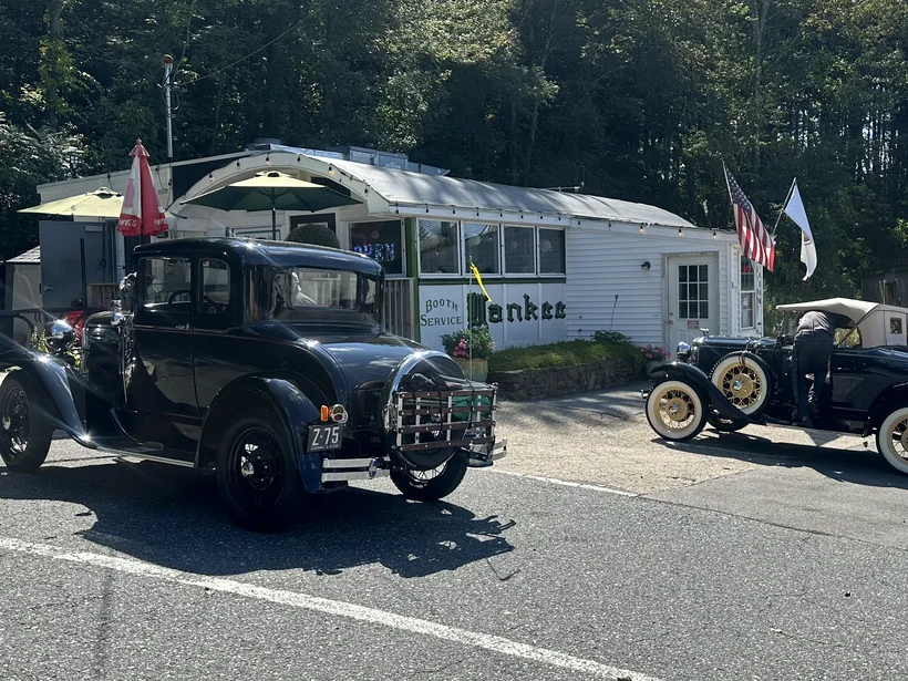 Two black Model A Fords pulled up outside the diner, with more antique cars parked further along the lot.